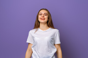 Obraz premium portrait of beautiful brunette young woman with clean skin, natural makeup looking at camera with big grin, standing over purple background