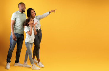 Wow offer. Full body length portrait of excited black family looking and pointing at copy space on yellow background - Powered by Adobe