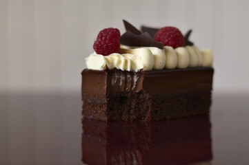 Delicious cake with two raspberries and chocolate crispy pieces on top on dark red table