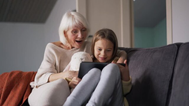 Surprised grandmother watching something on tablet with her granddaughter on the couch