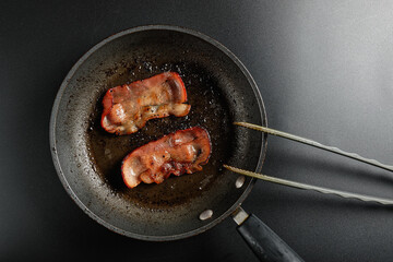 Fried breakfast bacon in a frying pan. With grill tongs. Flat lay with copy space.