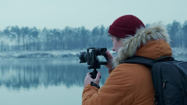 Adventure photographer takes pictures of a lake in the winter forest. on a professional camera