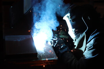 Skillful metal worker working with arc welding machine in factory while wearing safety equipment....