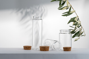 Small glass jars on white background with olive branch and shadow