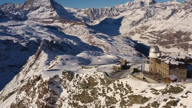 Aerial drone footage of the Matterhorn and the gornergrat ridge with its observatory and hotel above Zermatt in the alps in Switzerland on a sunny winter day. Shot with a backward tilt up motion