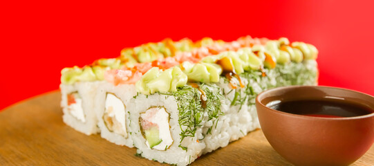 Sushi rolls near soy sauce. Set of tasty sushi rolls with cheese topped with sauce served on wooden table against red background in light room