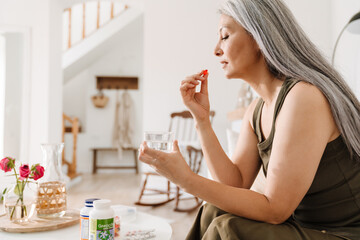 Mature asian woman taking her medication while sitting on couch