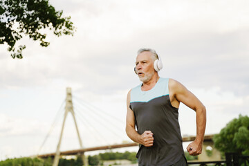 Grey senior sportsman listening music with headphones while running