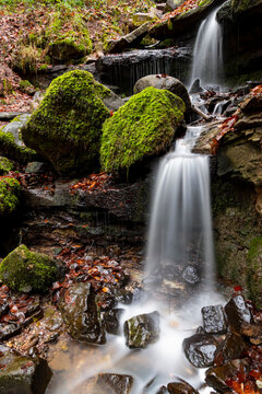 Cascades &ldquo;Heslacher Wasserf&auml;lle&ldquo; of a small creek with moss, wet rocks and brown foliage on a winter day in a forest near Stuttgart Vaihingen Germany with longtime exposure and blurred waterfalls.