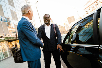 Multiracial men smiling and handshaking while standing by taxi