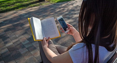An adult girl holds a book in her hands and takes pictures with a smartphone, they are in a blurred background. Close-up. Selective focus.