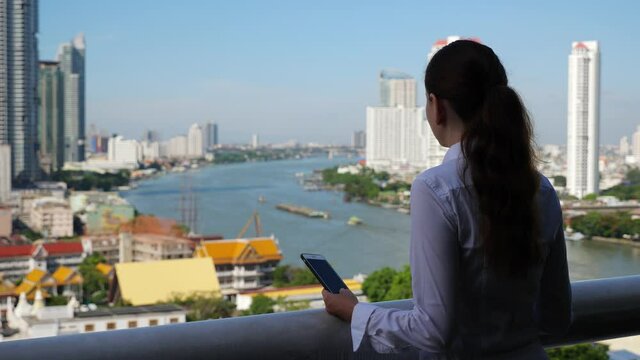 Reflective mood, business woman stand in shadow at balcony on high floor and look to city, view from back, blurred background. Caucasian person take pause to think during duty trip to Bangkok