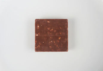 A piece of milk chocolate with nuts lies on a white plate. Minimalism, top view