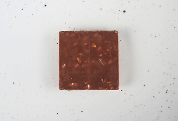 A piece of milk chocolate with nuts lies on a white plate. Minimalism, top view