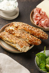 Savoury breakfast ingredients: brown lye bread sticks garnished with oats , pork slices prosciutto, hard cheese gouda and fresh greens on wooden boards