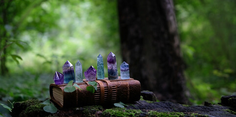 witch book and quartz minerals on dark natural forest background. Healing crystals of fluorite,...