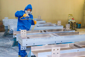 The painter is working to painting the steel structure with spray gun at industrial factory - obrazy, fototapety, plakaty