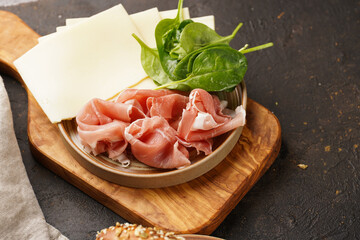 Savoury breakfast ingredients: brown lye bread sticks garnished with oats , pork slices prosciutto, hard cheese gouda and fresh greens on wooden boards