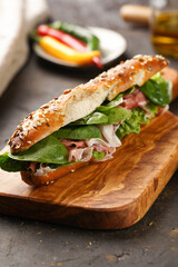 Long sandwich in brown lye bread sticks garnished with oats , pork slices prosciutto, hard cheese gouda and fresh greens on wooden boards