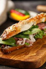 Long sandwich in brown lye bread sticks garnished with oats , pork slices prosciutto, hard cheese gouda and fresh greens on wooden boards