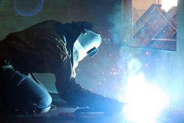 Obraz na płótnie Canvas Skillful metal worker working with arc welding machine in factory while wearing safety equipment. Metalwork manufacturing and construction maintenance service by manual skill labor concept.