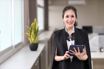 Portrait of confident and beautiful young asian businesswoman with happy emotion standing and using tablet in modern office. Success business concept