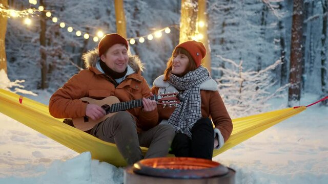 Couple guy with a girl sitting by the fire with a singing fun with a guitar winter. festive new year mood