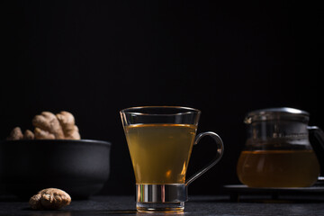Taza de té de jengibre con tetera sobre una mesa de madera negra