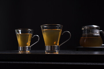 Dos tazas de té caliente de jengibre con tetera sobre una mesa de madera negra