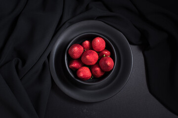 Fresas rojas en una placa negra sobre un fondo negro. Vista superior
