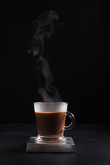 Café caliente y humeante en taza de vidrio sobre fondo negro. Aislado