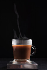 Café caliente y humeante en taza de vidrio sobre fondo negro. Aislado