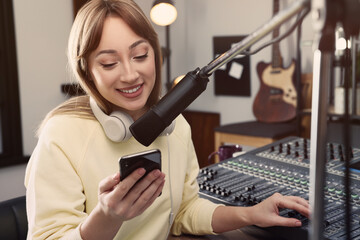Woman with smartphone working as radio host in modern studio
