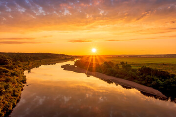 Scenic view at beautiful sunset or sunrise on a shiny river with green bushes on sides, golden sun...