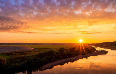 Scenic view at beautiful sunset or sunrise on a shiny river with green bushes on sides, golden sun rays, calm water ,deep blue cloudy sky and forest on a background, spring landscape