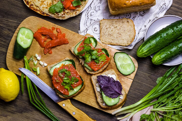 Sandwiches with salmon and greens. Sandwich with cottage cheese and basil and cucumber. Dark background.