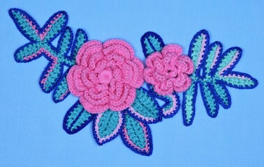 A decorative arrangement of handmade flowers and leaves on a blue crepe paper background.
