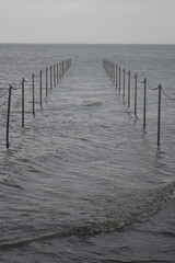 Fototapeta premium Stone groin (groyne) leading into the North Sea during high tide on a cloudy day (vertical image), Burhave, Lower Saxony, Germany