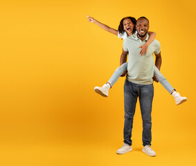 Joyful african american dad giving piggyback ride for daughter, girl pointing at free space on...