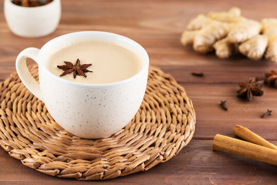 Masala tea with milk, anise, cinnamon, ginger, pepper in a cup on a wooden table. Selective focus.