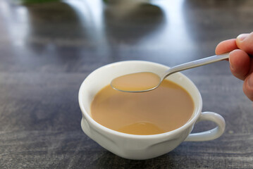 Coffee with milk in a white mug. The hand stirs the cofee with a spoon. A drop of coffee falls into a mug. close up