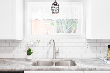Kitchen sink detail shot with a marble countertop, white cabinets, stainless steel faucet and sink,...