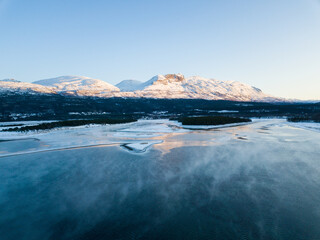 Aerial drone view of a snowy and icy lake in Norway during sunset