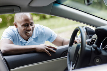 Happy african american man customer looking inside new car