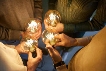 Team of four intelligent people together holding bright, shining, glowing Edison light bulbs as...