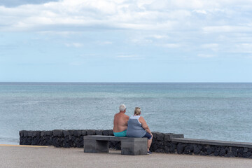 Una pareja de personas mayores sentadas en un banco mirando el mar en una playa de Lanzarote.