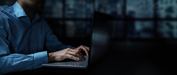 businessman working on laptop in dark office at night. banner copy space