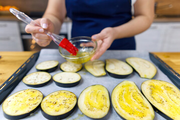 brushing with oil sliced eggplant on a baking tray. grilled eggplant appetizer cooking process. close up