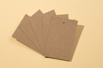 Five cardboard blank label tags for clothes with tiny holes in upper part placed on each other resembling fan in center with shadows falling on flesh colored background. Tag mock up. Copy space.