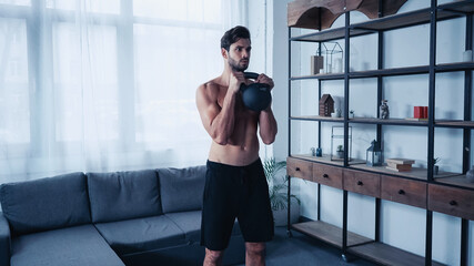 young sportsman in shorts training with heavy kettlebell at home